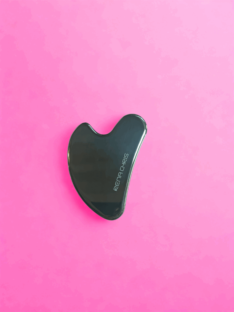 Gua sha en acier inoxydable Rena Chris sur fond rose pour massage facial lifting naturel
